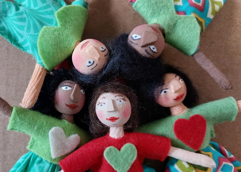 Foto colorida de cinco bonecas artesanais, com características diferentes entre elas. 