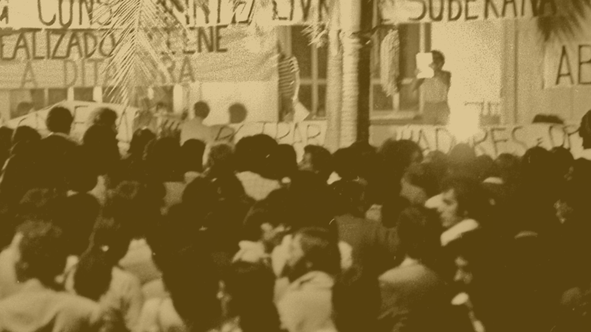 Foto presente na exposição Ocupações Memorial: Resistências na PUC-SP, registrada durante os anos 1960. A foto mostra uma manifestação de estudantes da PUC contra a ditadura. Há dezenas de pessoas e cartazes com palavras de ordem contra a ditadura.