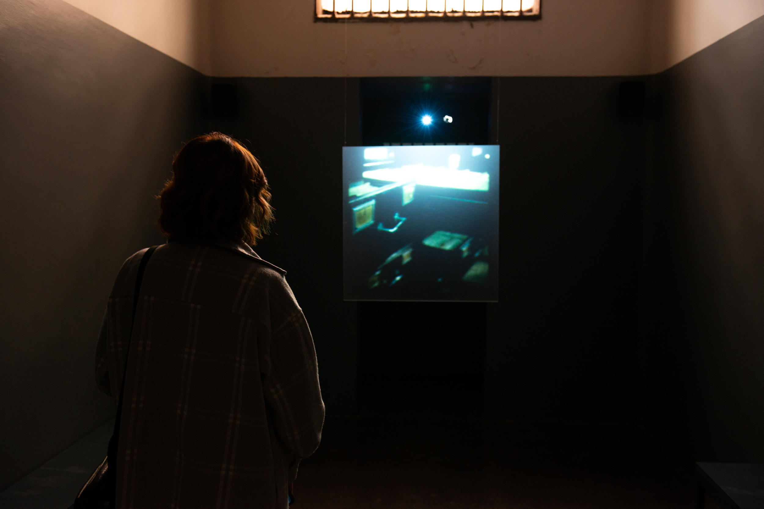 Mulher de costas para câmera, observando material em vídeo da exposição de Longa Duração do Memorial da Resistência de São Paulo que apresenta ao público o que restou do espaço carcerário do (DEOPS/SP).